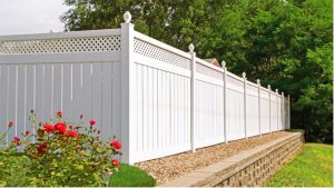 Vinyl Fences Cherry Hill NJ White vinyl fence in a yard above bricks and rocks with red flowers to the left of the fence